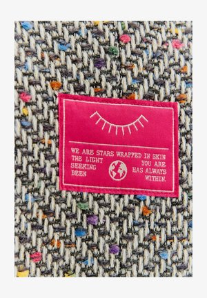 Etykieta tekstylna na wielokolorowej tkaninie tkanej; fioletowe, niebieskie, pomarańczowe plamki na szarym tle; etykieta z różowego materiału z białym tekstem.