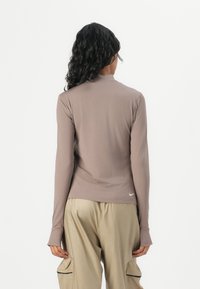 Langärmliges, figurschmeichelndes Rollkragenoberteil in Taupe, aus glattem, dehnbarem Stoff. Mit einem subtilen Nike-Logo am Saum und Daumenlöchern in den Ärmeln.