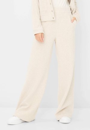 Pantalons de lounge larges, couleur crème, en tissu doux et texturé avec une taille haute et des poches latérales, associés à des baskets blanches.