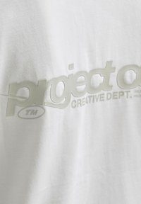 Biała bawełniana koszulka z połyskującą, wypukłą grafiką w jasnoszarym kolorze, z napisem "project" oraz "CREATIVE DEPT." i symbolem znaku towarowego.