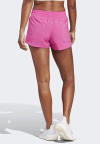 Pantalones cortos deportivos rosas con cintura elástica, confeccionados en una tela suave y ligera, con un dobladillo curvado para facilitar el movimiento. Combinados con zapatillas blancas.