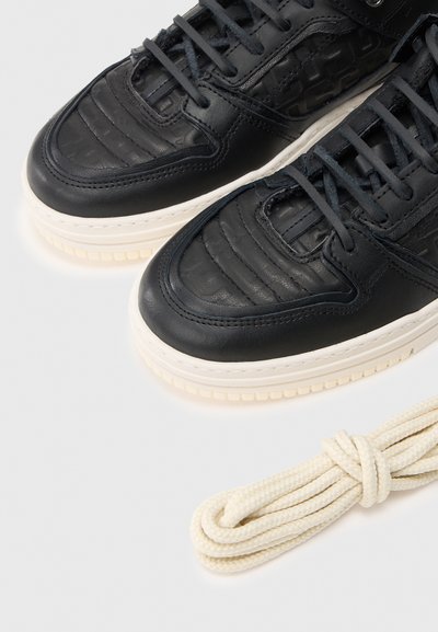 Czarne skórzane sneakersy mają teksturowane panele, przeszycia oraz masywną kremową podeszwę. W komplecie znajduje się skręcony kremowy sznurowadło.