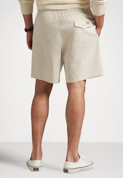 Calções bege às quadrículas com cintura elástica, um bolso traseiro e tecido texturizado; usados com sapatos de lona brancos.