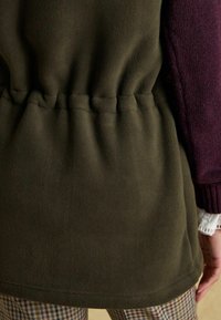 Fleece bunda so sťahovacím pásom, s tmavozeleným telom a vínovými pletenými rukávmi. Hladká textúra, jednoduchý dizajn.