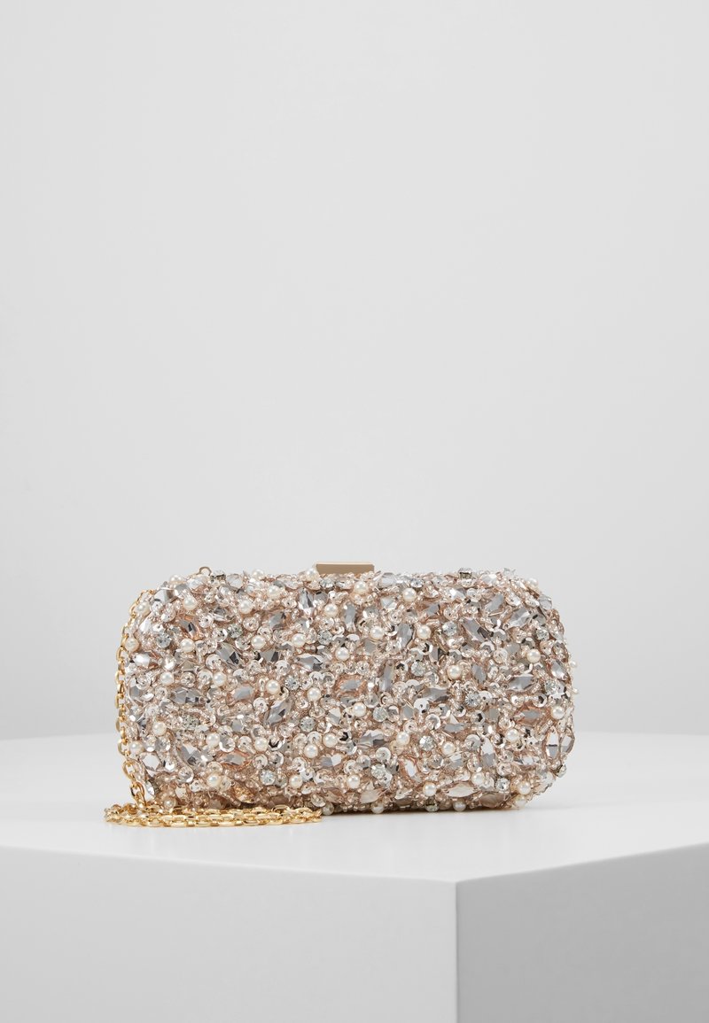 Pochette de soirée recouverte de petites perles, de cristaux clairs et de perles dorées avec une bandoulière chaîne dorée sur un piédestal blanc.