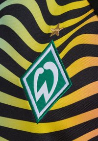 Grön och vit logotyp på ett svart och gult randigt tyg med en strukturerad yta; har en guldstjärna ovanför logotypen.