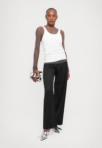 White tank top, sheer brown long sleeves, black wide-leg trousers, silver pointed-toe shoes, holding a transparent handbag.