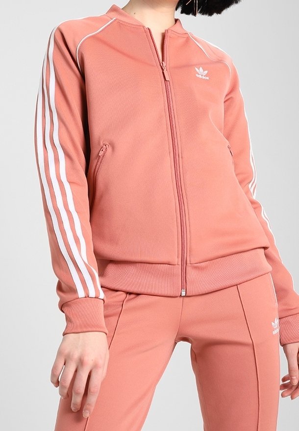 Pink zip-up athletic jacket with white stripes on sleeves, made of smooth fabric, featuring a stand-up collar and hidden side pockets.