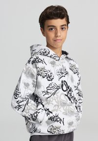 Felpa con cappuccio bianca con stampe in stile graffiti nere. Presenta una tasca a marsupio e polsini a costine. Tessuto morbido con una vestibilità rilassata.