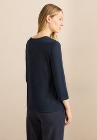 Dunkelblaues Oberteil mit Dreiviertelärmeln aus weichem Stoff, mit runder Ausschnittlinie und lässiger Passform, leicht seitlich präsentiert.