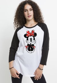 T-shirt bianca in cotone con maniche raglan nere, con una grafica di un topo cartone animato che indossa un fiocco rosso a pois e un vestito.