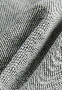 Tessuto grigio intrecciato che mostra un primo piano di una superficie testurizzata con motivi diagonali e fili a contrasto in diverse sfumature.