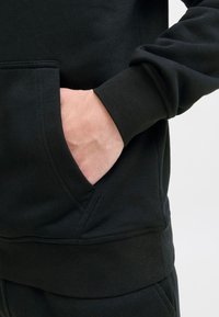 Zwarte sweatshirt met een kangoeroezak en geribde manchetten. Gladde textuur met een eenvoudig, strak ontwerp.