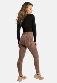Leggings a vita alta, marrone maculato, con dettagli cuciti e due tasche posteriori. Indossati con una maglia nera attillata a maniche lunghe e sneakers.