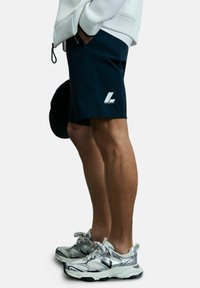 Marineblaue Sportshorts mit einem weißen Logo, kombiniert mit silbernen Sneakers mit schwarzen Akzenten und strukturierten Details.