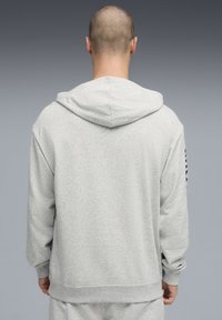 Sweat à capuche gris avec une finition texturée, doté d'une capuche ajustable par cordon, de manches longues et d'une coupe décontractée. Comprend un détail logo sur la manche gauche.