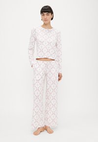 Biela pyžamová súprava s dlhými rukávmi, krátkym vrchom a nohavicami na celý úväzok, zdobená ružovým kvetinovým vzorom. Vyrobená z jemnej, ľahkej látky.