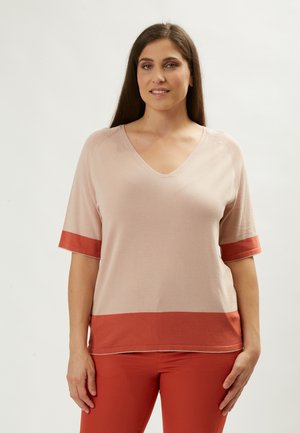 Top corto de color beige claro con cuello en V profundo y dobladillo y puños en color óxido contrastante. Textura suave, ajuste casual, sin patrones visibles.