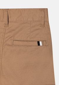 Pantaloni in cotone color beige con una tasca posteriore caratterizzata da un dettaglio a righe nere, bianche e nere. Texture liscia e design su misura.