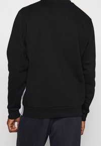 Sweat-shirt noir avec un col rond, des manches longues et des poignets côtelés. Les panneaux latéraux présentent un accent contrastant blanc. Tissu doux et texturé.