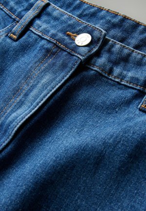 Džínsy s modrým odtieňom, so strieborným zapínaním a viditeľnými švami. Mäkká textúra a klasický dizajn s piatimi vreckami.