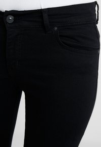 Černé džínové kalhoty z denimu mají přiléhavý střih s hladkou texturou, přední kapsy a zapínání na jeden knoflík v pase.