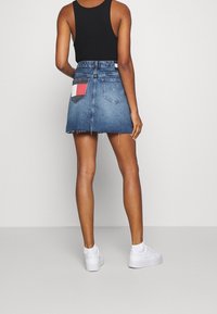 Jeanskjol med fransad nederkant, med en färgblockspatch på bakfickan. Bärs med en svart linne och vita sneakers.