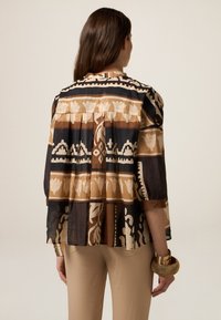 Bedruckte Bluse in erdigen Brauntönen und Schwarz mit floralem und geometrischem Muster. Taillenlänge, leichtes Material, Dreiviertelärmel.