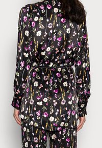 Black satin blouse with colorful floral print, featuring a belted waist, long sleeves, and a curved hemline.