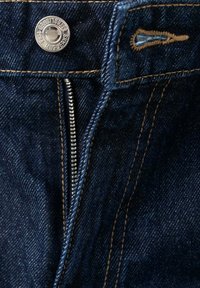 Denim jeans with a partially open metal zipper, metal button engraved with brand name, and visible buttonhole stitching.