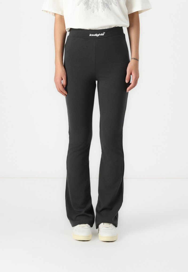 Pantaloni neri a zampa d'elefante con cintura elastica, dotati di un'etichetta con logo. Il materiale sembra morbido e elasticizzato, progettato per una silhouette aderente.