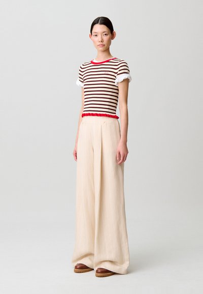 Maglietta a righe con maniche corte bianche, bordo rosso e orlo arricciato abbinata a pantaloni beige a vita alta, a gamba larga, con righe verticali.