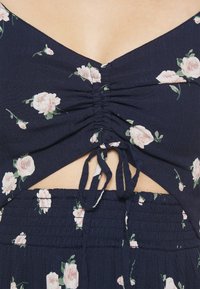 Marineblaues Blumenkleid mit gerafftem Oberteil, Ausschnitt und Schleifenverschluss. Weicher Stoff mit pinken Rosenmustern.