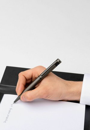 Metallstift mit strukturiertem Finish, der von einer Hand gehalten wird, während er auf einem weißen Blatt Papier in einem schwarzen Ordner schreibt.