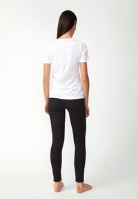 Bílý tričko s krátkým rukávem a klasickým kulatým výstřihem, kombinované s černými úzkými džíny, pohled zezadu. Čistý, minimalistický design.