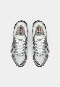 Τα παπούτσια για τρέξιμο Asics GT-2160 διαθέτουν επάνω μέρος από διχτυωτό ύφασμα σε λευκό και γκρι, με κόκκινες λεπτομέρειες, στρογγυλή μύτη και αντίθετη μαύρη σόλα.