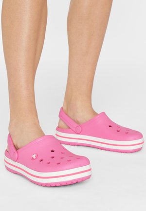 Sabots roses en matériau synthétique, dotés de trous de ventilation, d'une sangle à l'arrière et d'une semelle plateforme à rayures blanches.