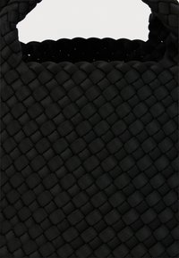 Μαύρη υφασμένη τσάντα tote από υλικό με υφή, με στιβαρό, πλεγμένο σχέδιο και στρογγυλεμένες λαβές για εύκολη μεταφορά.