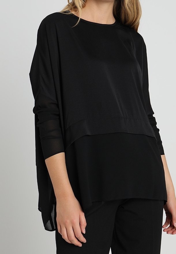 Top nero a strati con vestibilità rilassata, maniche lunghe trasparenti e materiale liscio con un orlo posteriore leggermente più lungo.