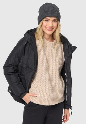 Black padded jacket with a zip front, worn over a beige chunky knit sweater. Grey ribbed beanie, smooth texture, casual style.