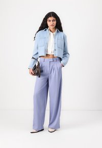 Τζάκετ denim σε ανοιχτό μπλε, άσπρη πουκάμισο με γιακά, και παντελόνι με φαρδιά πόδια σε λεβάντα με ρίγες. Αξεσουάρ: μικρή σκούρα τσάντα ώμου.