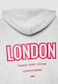 Sweat à capuche gris avec un motif graphique sur le devant indiquant "LONDON" en lettres roses audacieuses, avec "ENERGY SPORT CENTER", "COVENTGARDEN" et "1990" en dessous.
