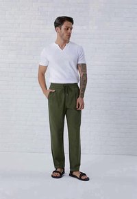 Hvit V-hals T-skjorte kombinert med mørkegrønne bukser med elastisk liv og snor. Sorte sandaler fullfører antrekket.