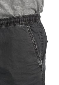 Pantalones cortos negros con cintura elástica, bolsillos laterales y una etiqueta de tela. Textura suave y lisa con un diseño casual.