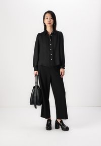 Black button-up shirt with textured fabric, long sleeves, and pearlescent buttons, paired with wide-leg black trousers and chunky black heels.