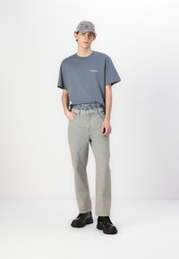 Ljust blå oversized t-shirt, grå keps med färgglada mönster, ljusa denimbyxor och svarta kraftiga stövlar. Minimalistisk design, avslappnad passform.