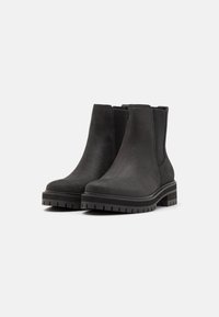 Botines negros de tobillo hechos de piel lisa, con paneles laterales elásticos, una suela de goma gruesa y un diseño de punta redonda.