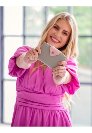 Light gray wallet with a pink flap, featuring a snap closure and embossed text. Smooth texture with rounded edges, held by a person.