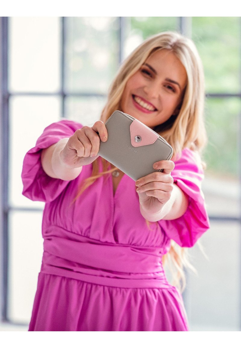Light gray wallet with a pink flap, featuring a snap closure and embossed text. Smooth texture with rounded edges, held by a person.