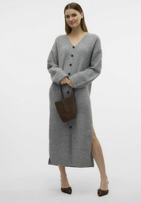 Cárdigan gris largo y abotonado con escote en V, mangas oversized y aberturas laterales. Combinado con un bolso pequeño marrón y zapatos marrones de puntera puntiaguda.